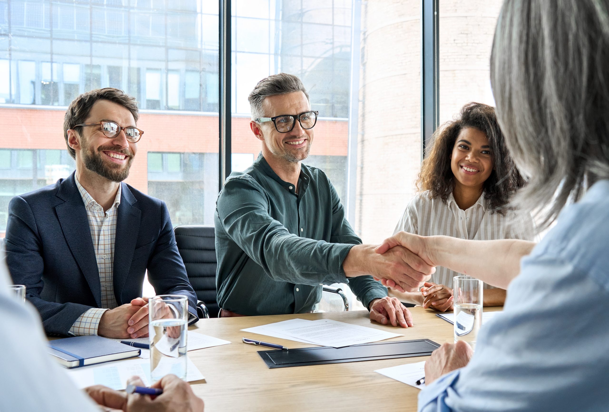 Happy businessman and businesswoman shaking hands at group board meeting. Professional business executive leaders making handshake agreement successful company trade partnership handshake concept.