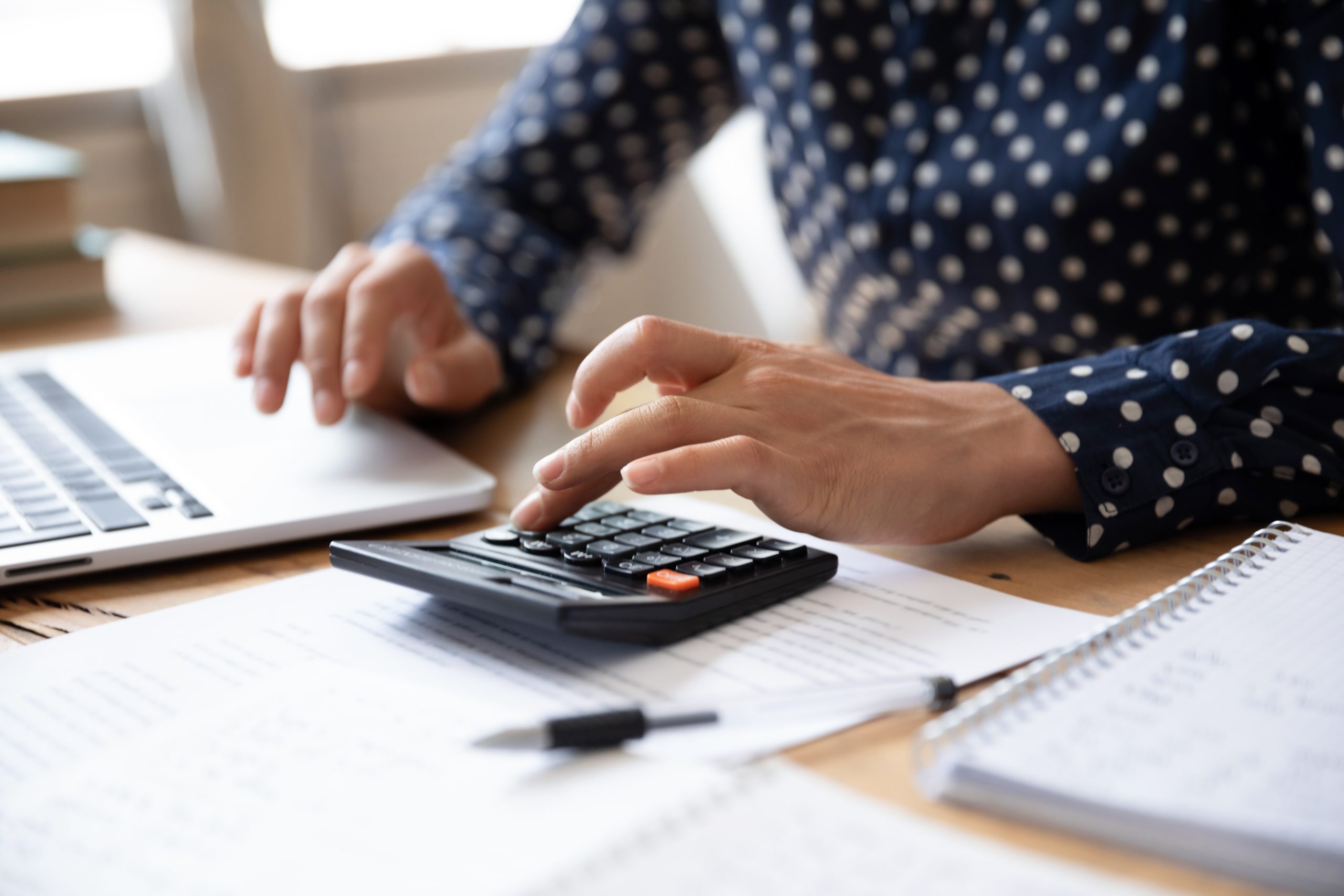 Person sitting at desk using calculator while also on laptop going over finances