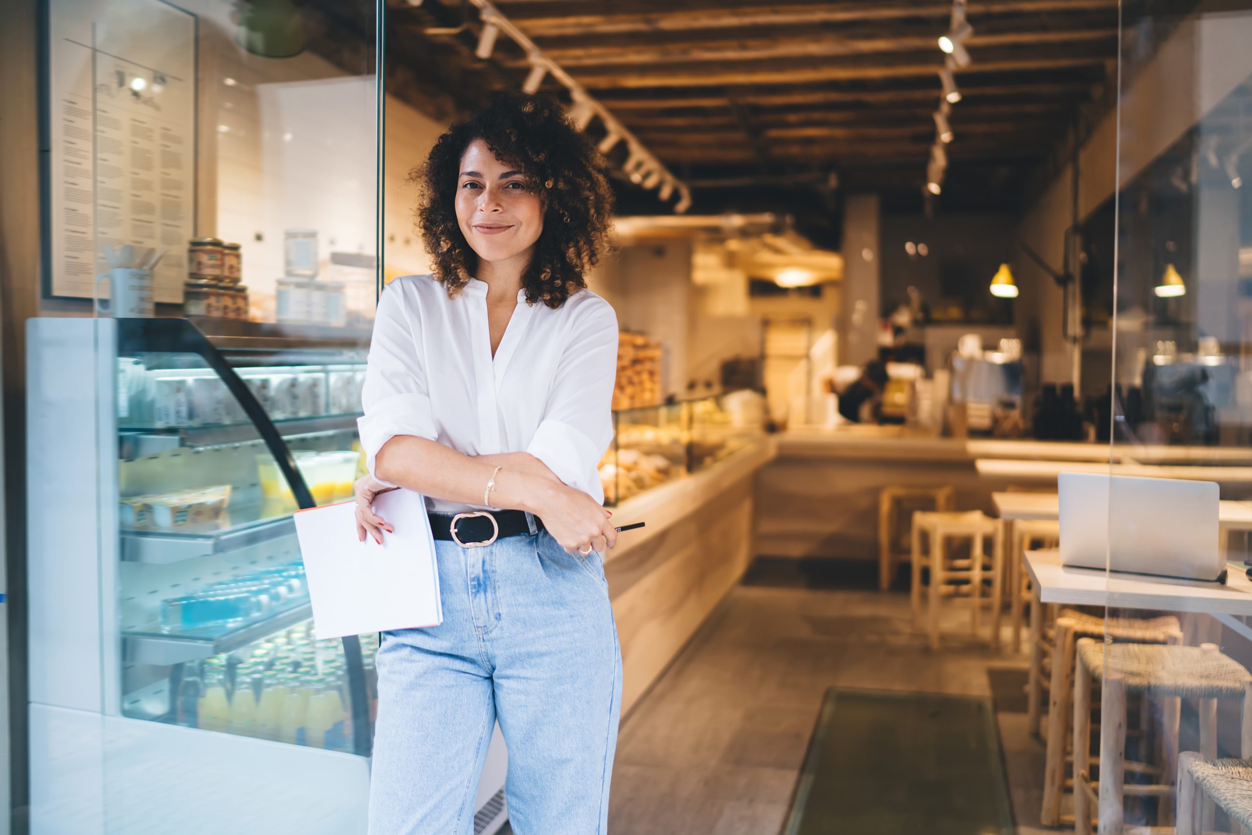 Portrait of prosperous manager of local bakery smiling at camera during work day in franchise takeaway cafe, happy woman with paper statistics enjoying time for improve own coffeehouse