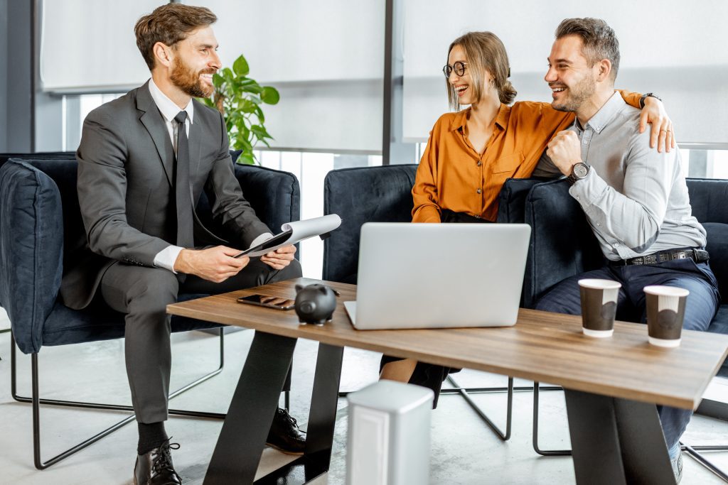 Happy young couple having a great deal with financial advisor or real estate agent at the luxury office.