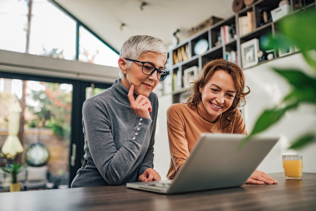 Two casual women looking at laptop indoors, portrait.